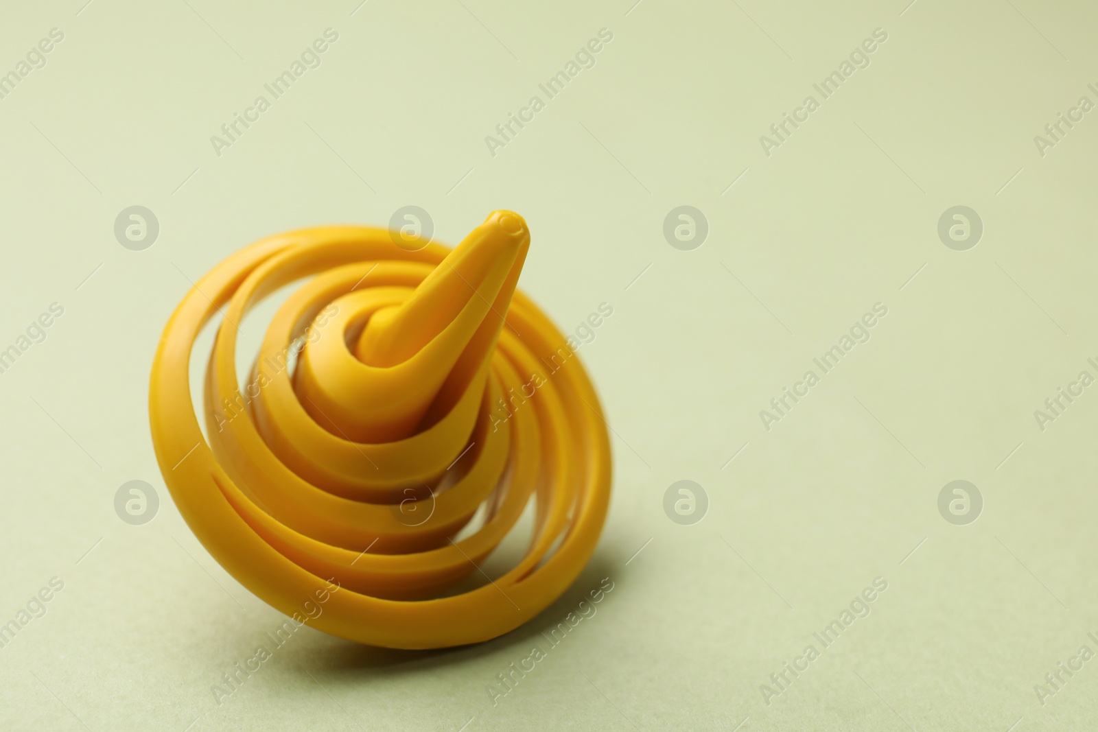 Photo of One yellow spinning top on green background, closeup. Space for text