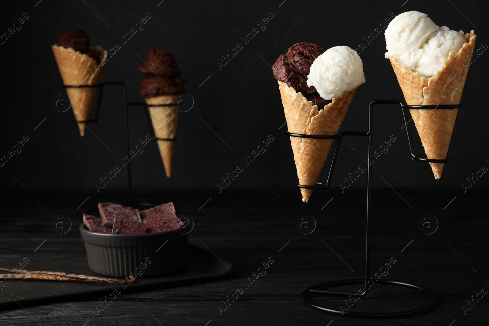 Photo of Ice cream scoops in wafer cones on black wooden table against dark background