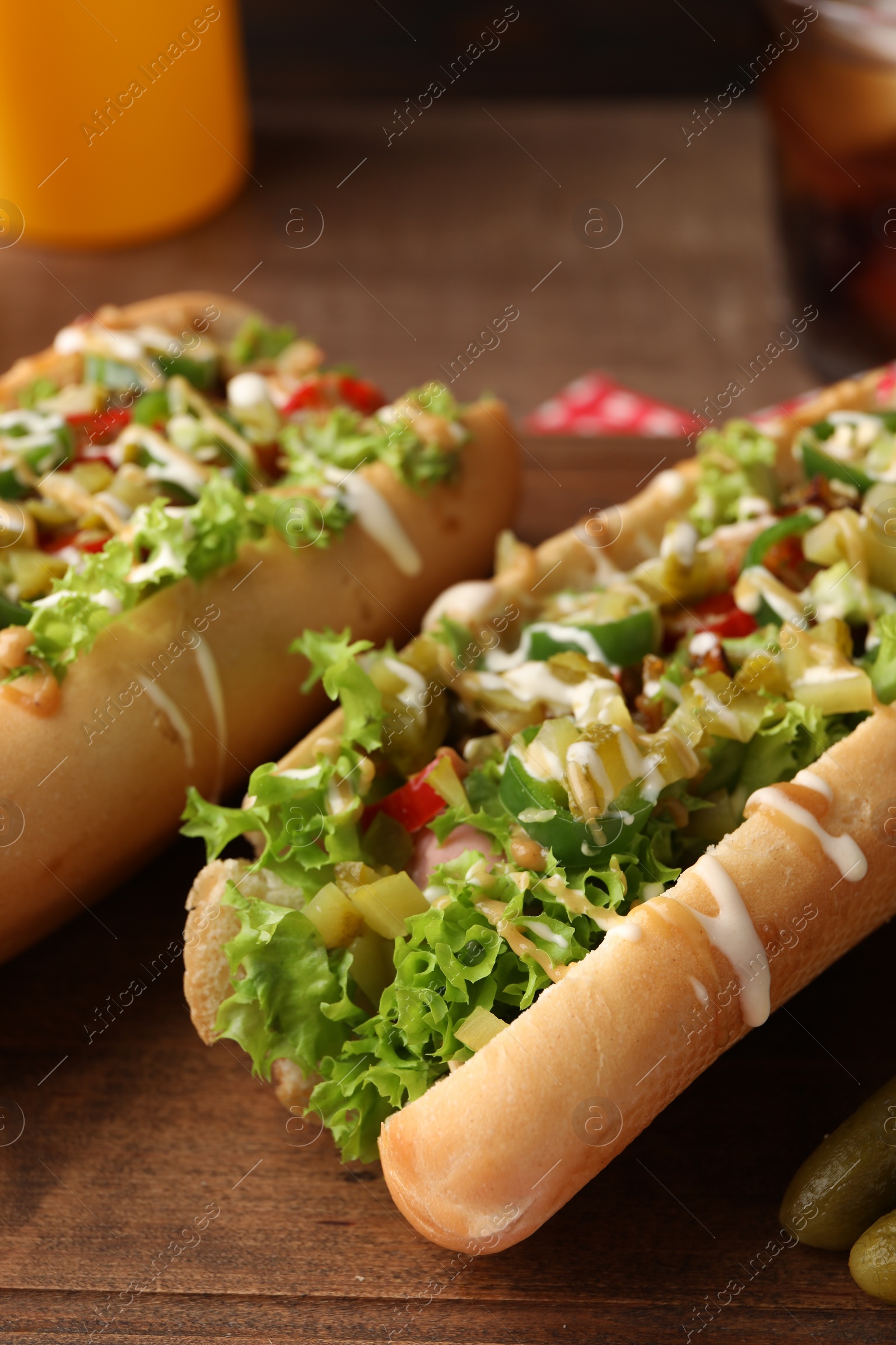 Photo of Tasty hot dogs with chili, lettuce, pickles and sauces on wooden table, closeup