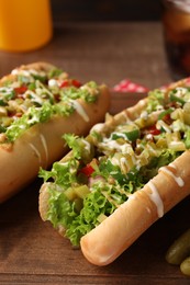Photo of Tasty hot dogs with chili, lettuce, pickles and sauces on wooden table, closeup