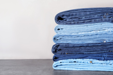 Photo of Stack of different jeans on grey table. Space for text