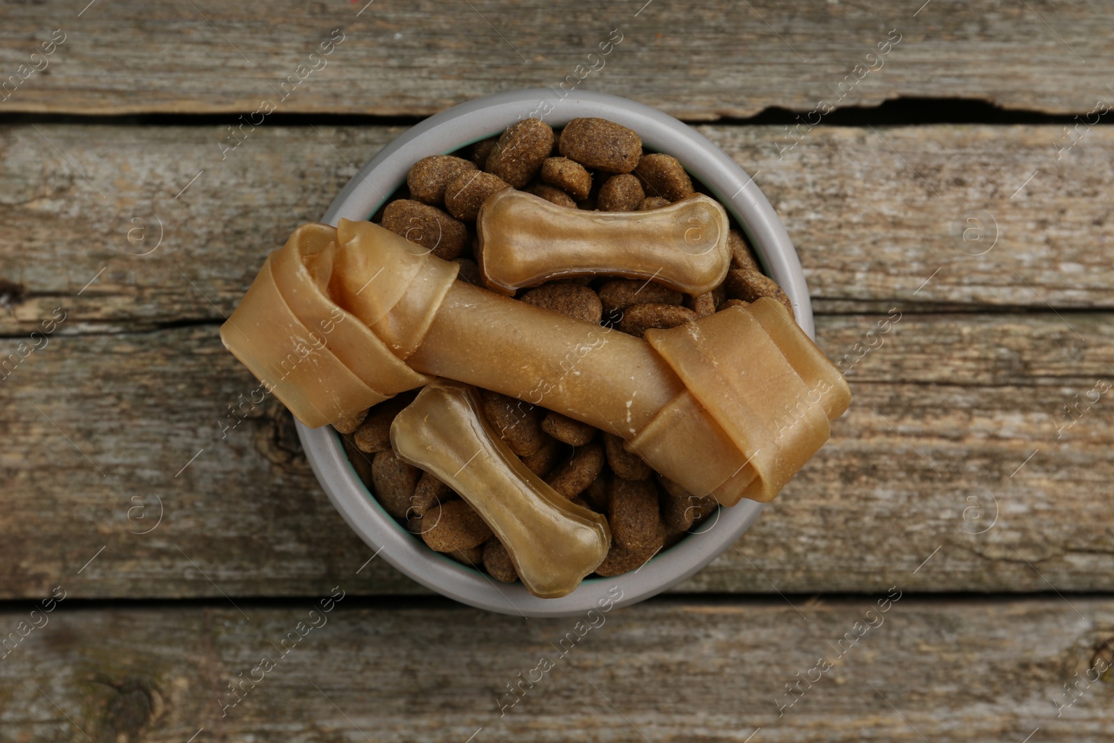 Photo of Dry dog food and treats (chew bones) on wooden floor, top view