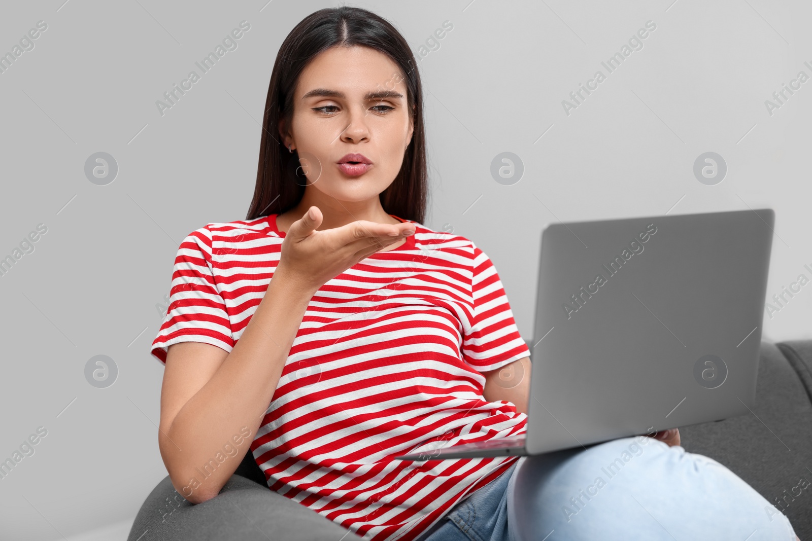 Photo of Young woman having video chat via laptop and blowing kiss on sofa in room