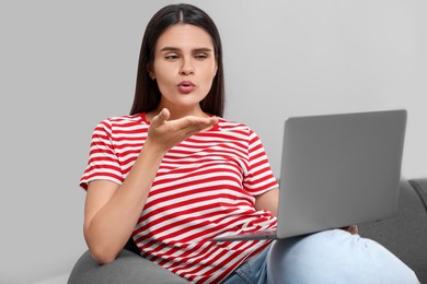 Photo of Young woman having video chat via laptop and blowing kiss on sofa in room