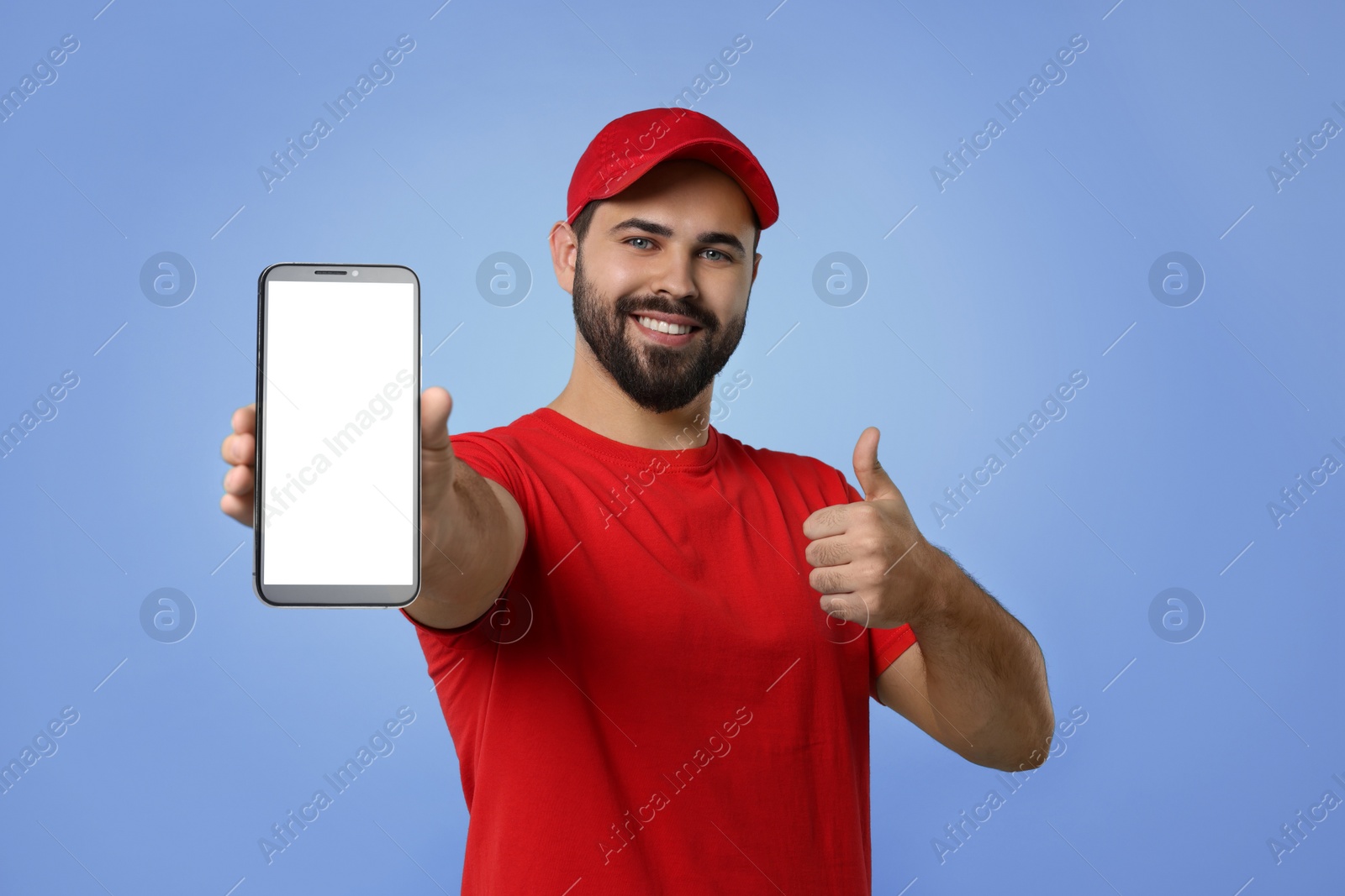 Image of Happy courier holding smartphone with empty screen and showing thumbs up on blue violet background