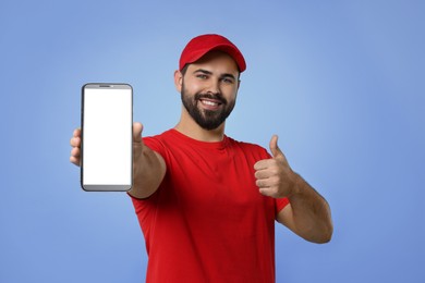 Happy courier holding smartphone with empty screen and showing thumbs up on blue violet background