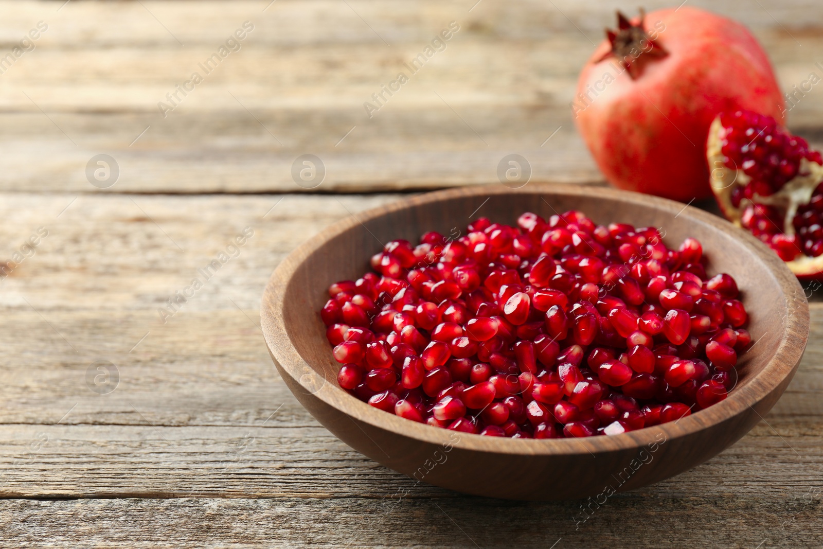 Photo of Ripe juicy pomegranate grains in bowl on wooden table. Space for text