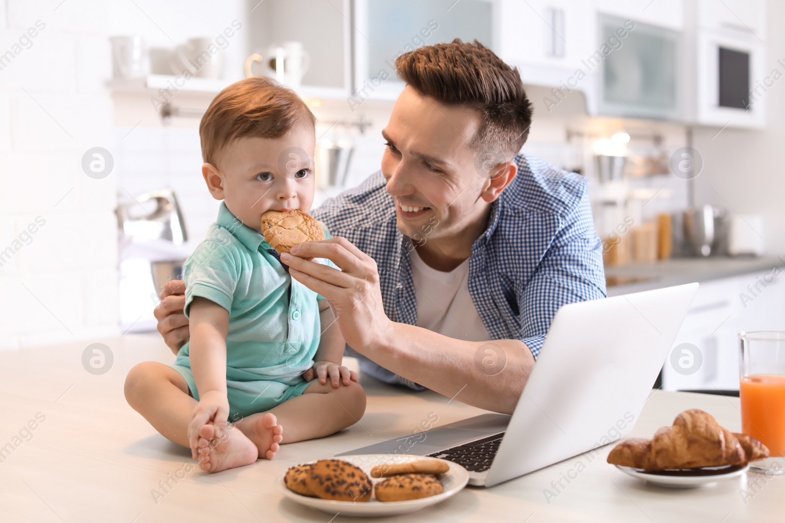 Photo of Young father and his cute little son with cookies in kitchen