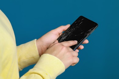 Woman holding damaged smartphone on light blue background, closeup. Device repairing