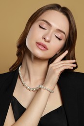 Photo of Young woman wearing elegant pearl jewelry on brown background