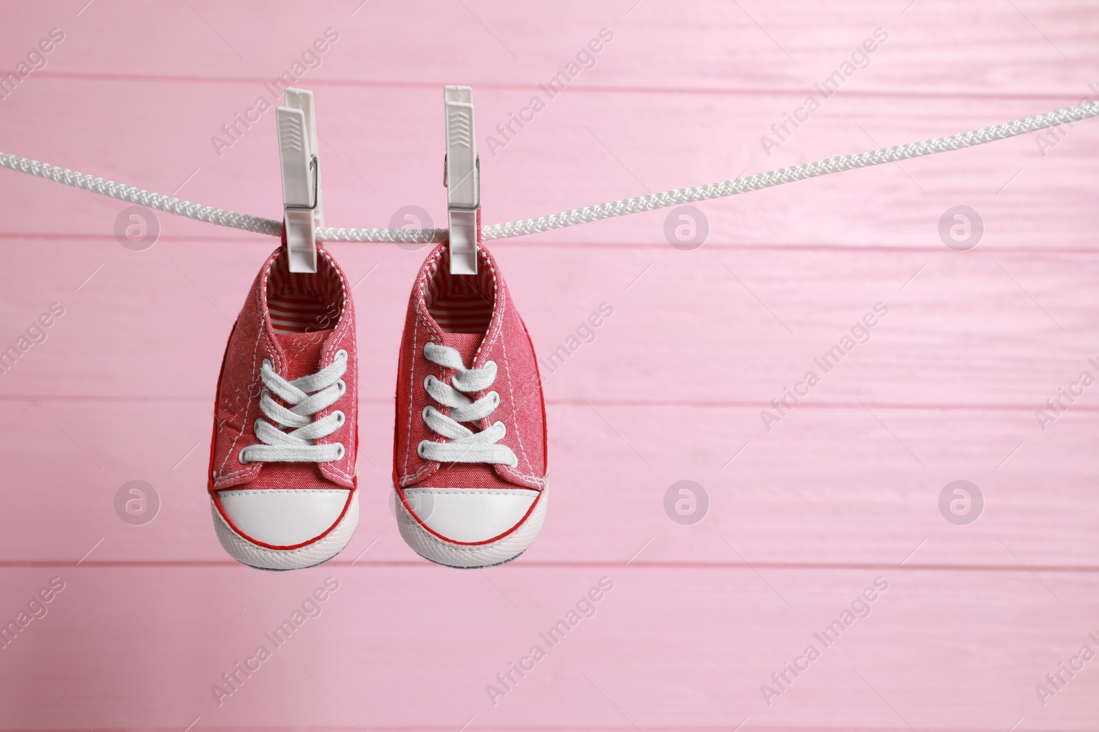 Photo of Cute baby sneakers drying on washing line against pink wooden wall. Space for text