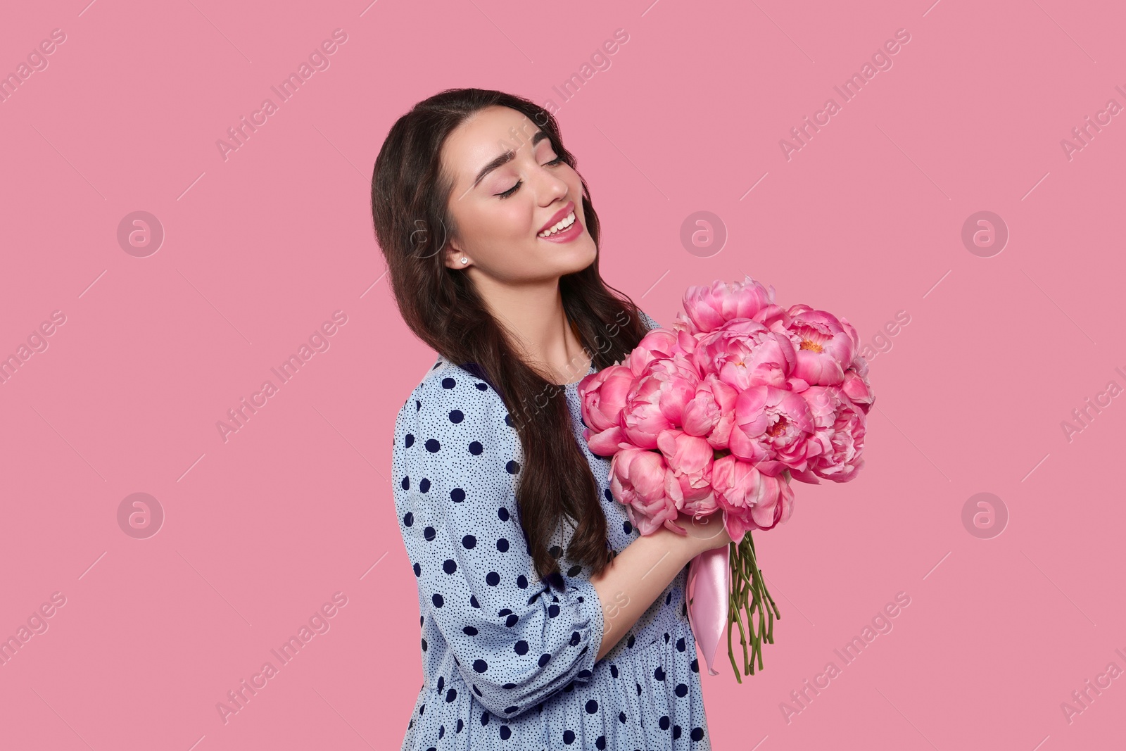 Photo of Beautiful young woman with bouquet of peonies on pink background