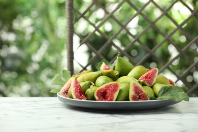 Cut and whole green figs on white marble table against blurred background, space for text