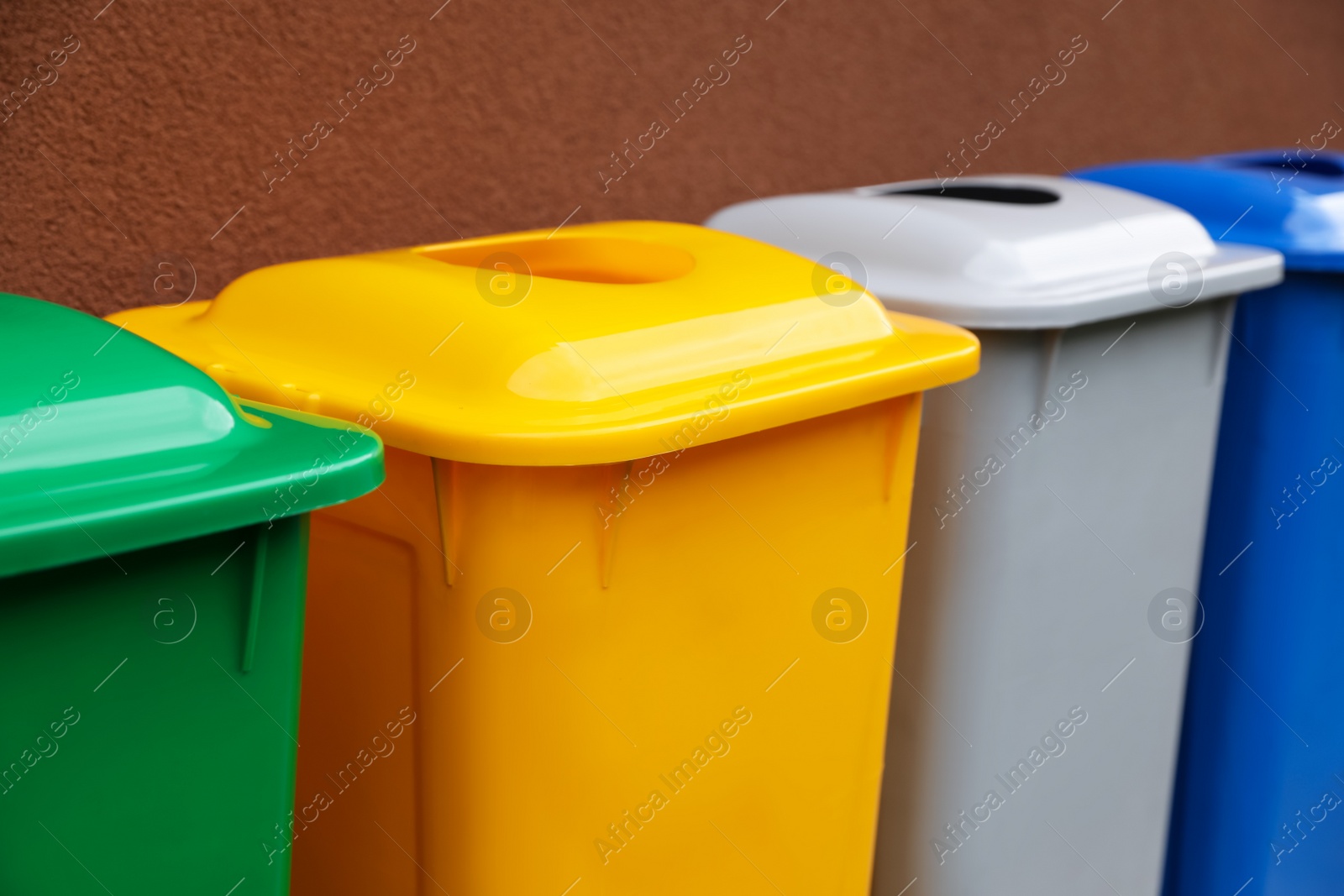 Photo of Many color recycling bins near brown wall, closeup