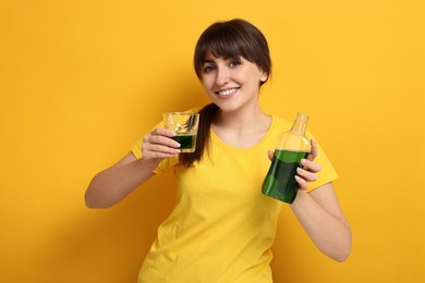 Young woman using mouthwash on yellow background