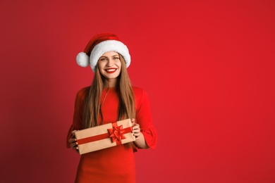 Young beautiful woman in Santa hat with gift box on color background. Christmas celebration