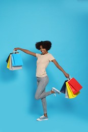 Photo of Happy African American woman with shopping bags on light blue background