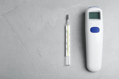 Photo of Non-contact infrared and mercury thermometers on light grey stone background, flat lay. Space for text