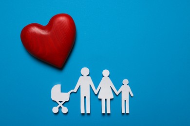 Photo of Paper family figures and red wooden heart on light blue background, flat lay. Insurance concept