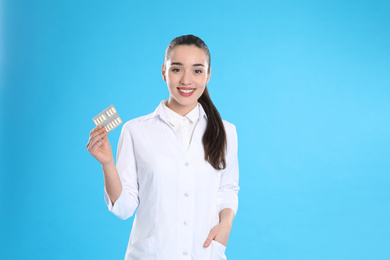 Professional pharmacist with pills on light blue background