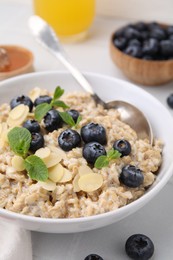 Photo of Tasty oatmeal with blueberries, mint and almond petals in bowl on white table, closeup