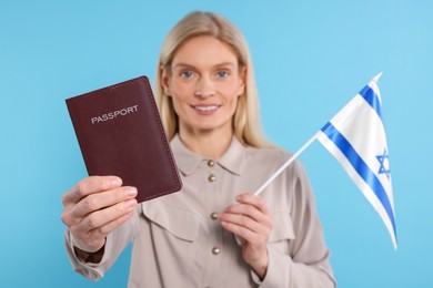 Photo of Immigration. Happy woman with passport and flag of Israel on light blue background, selective focus