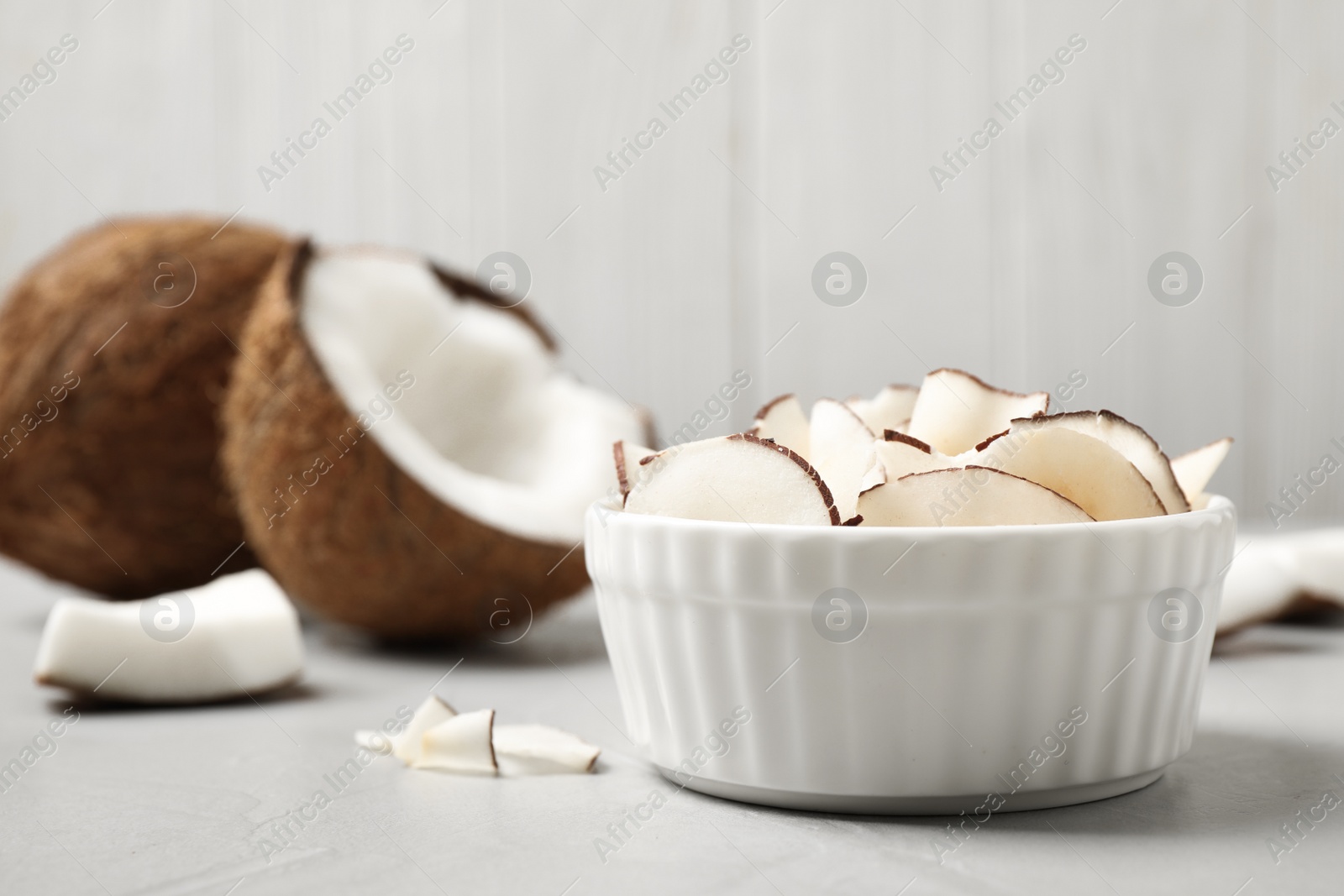 Photo of Tasty coconut chips on grey table against wooden background. Space for text