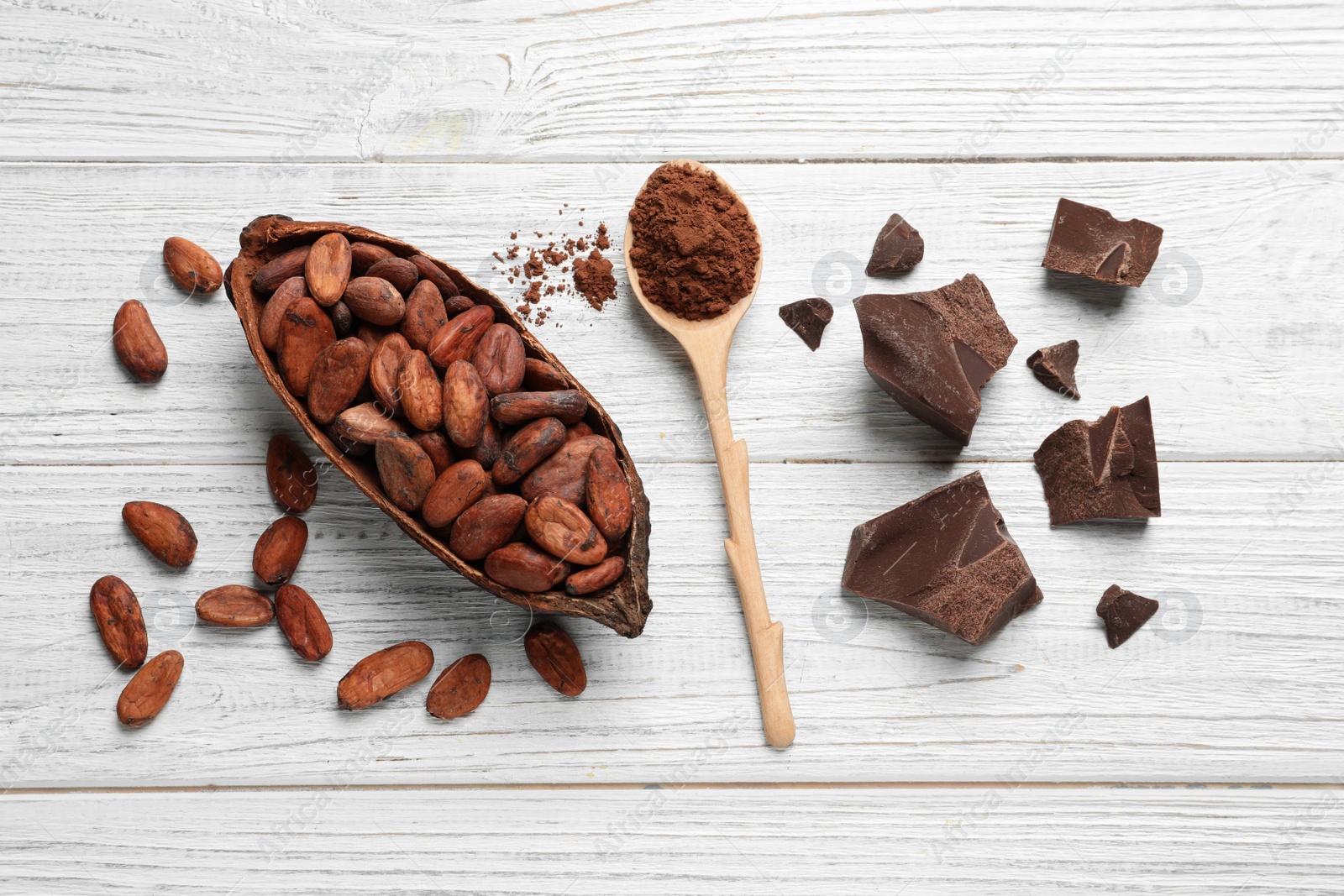Photo of Flat lay composition with cocoa beans, spoon of powder and chocolate on white wooden table