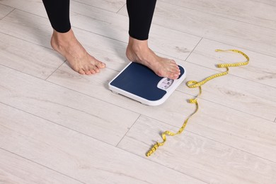 Woman stepping on floor scale and measuring tape at home, closeup. Weight control