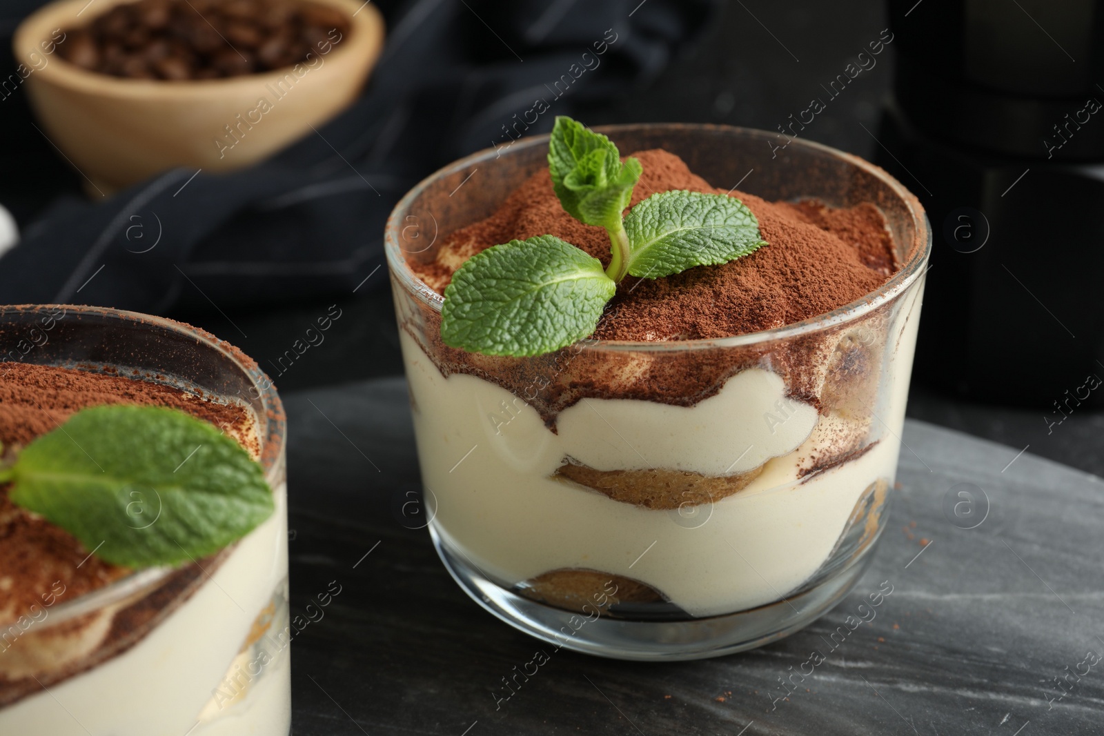 Photo of Delicious tiramisu in glasses and mint leaves on table, closeup