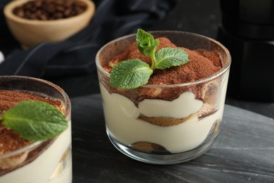 Delicious tiramisu in glasses and mint leaves on table, closeup