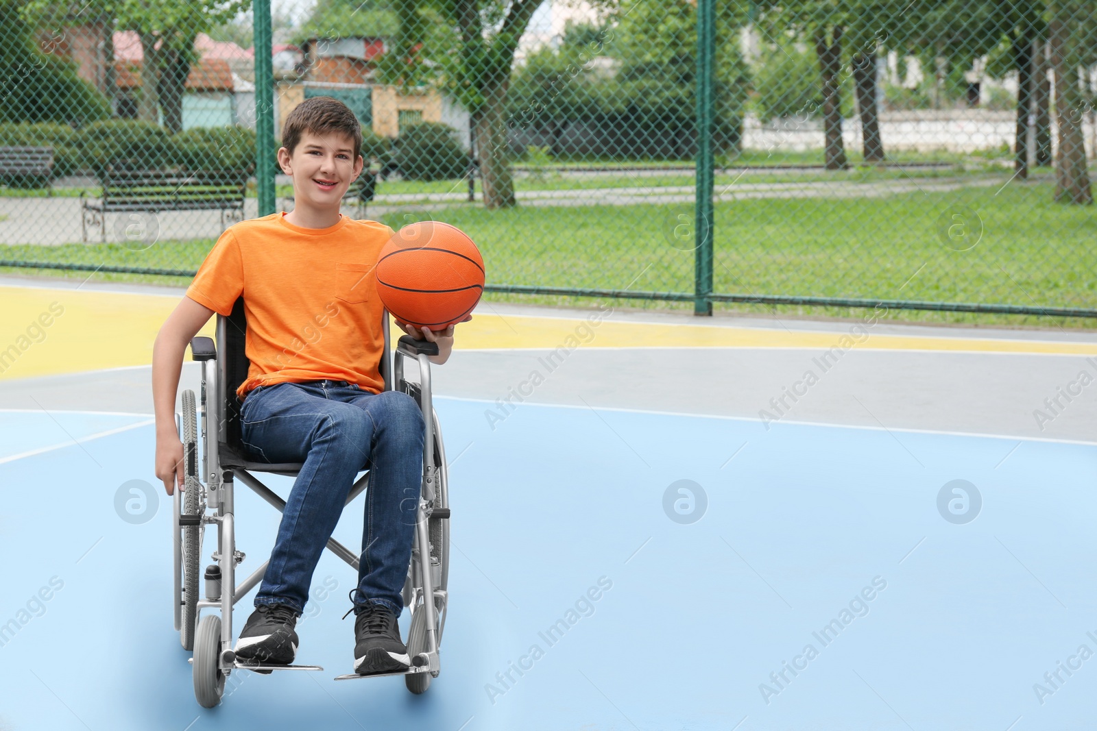 Photo of Disabled teenage boy in wheelchair with basketball ball at outdoor court