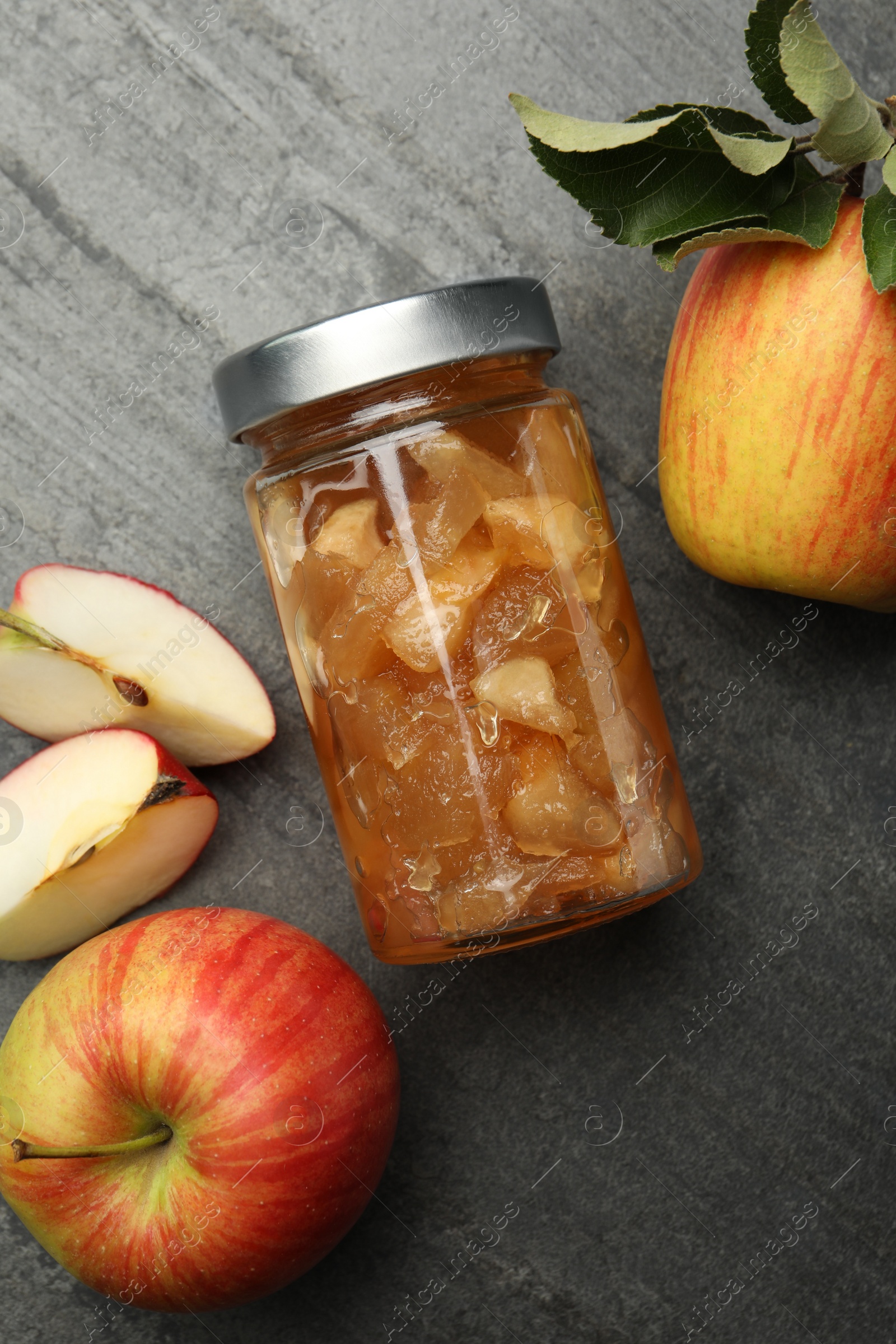 Photo of Tasty apple jam in glass jar and fresh fruits on grey table, flat lay