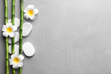 Spa stones, plumeria flowers and bamboo stems on light grey table, flat lay. Space for text
