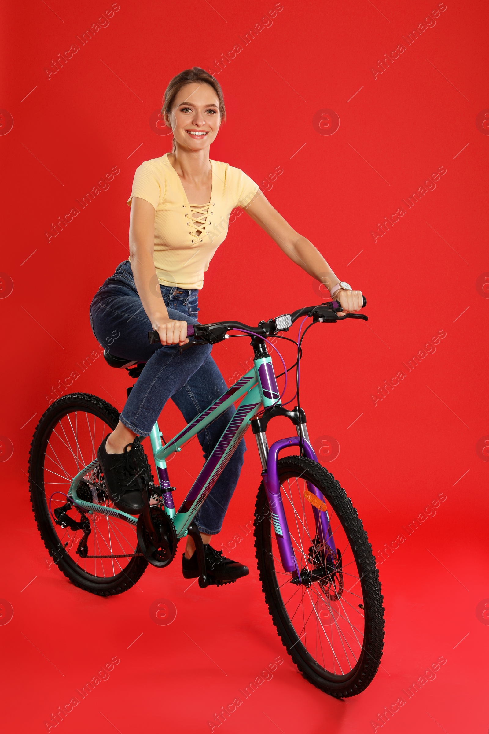 Photo of Happy young woman riding bicycle on red background