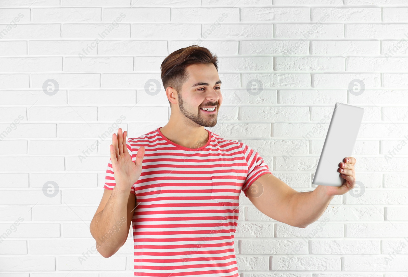 Photo of Man using tablet for video chat against brick wall