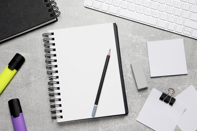 Photo of Open blank notebook, keyboard and stationery on light grey table, flat lay