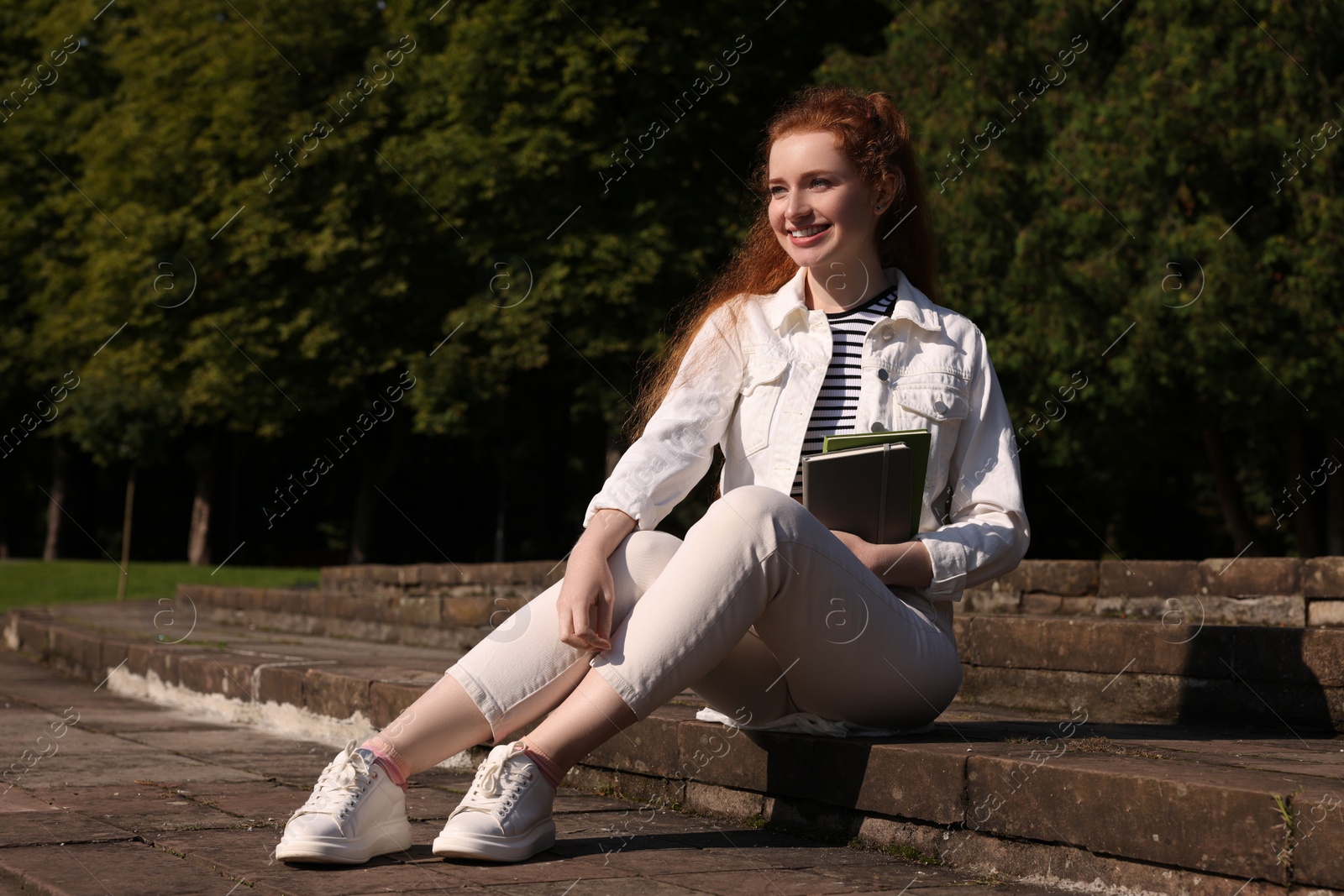 Photo of Happy young student with notebooks on steps in park