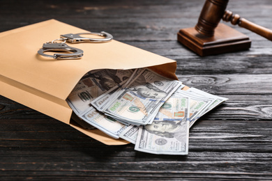 Envelope with dollar bills and handcuffs on black wooden table. Bribe concept