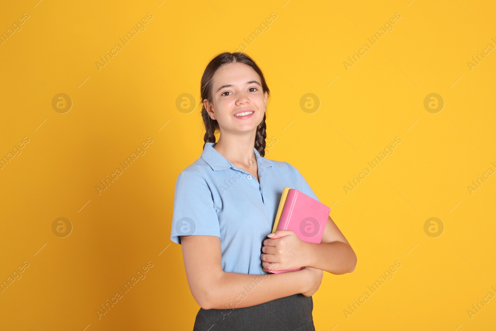 Photo of Teenage girl in school uniform with books on orange background