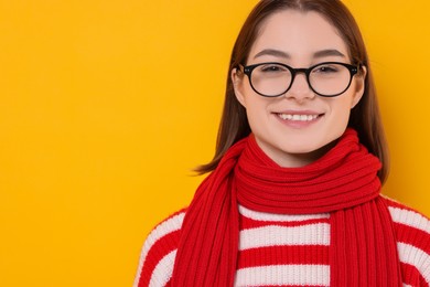 Photo of Beautiful woman in warm scarf and glasses on yellow background, space for text