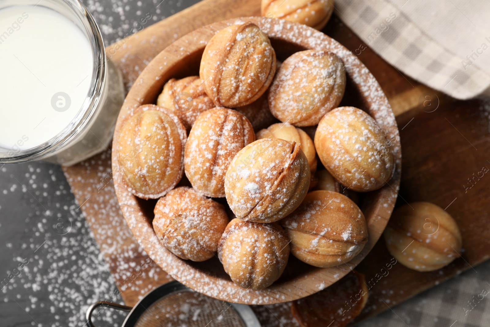 Photo of Delicious nut shaped cookies with powdered sugar and milk on black table, flat lay