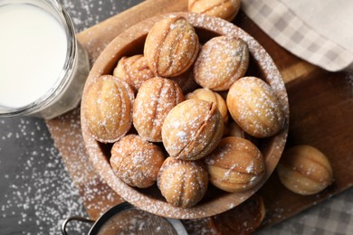 Photo of Delicious nut shaped cookies with powdered sugar and milk on black table, flat lay