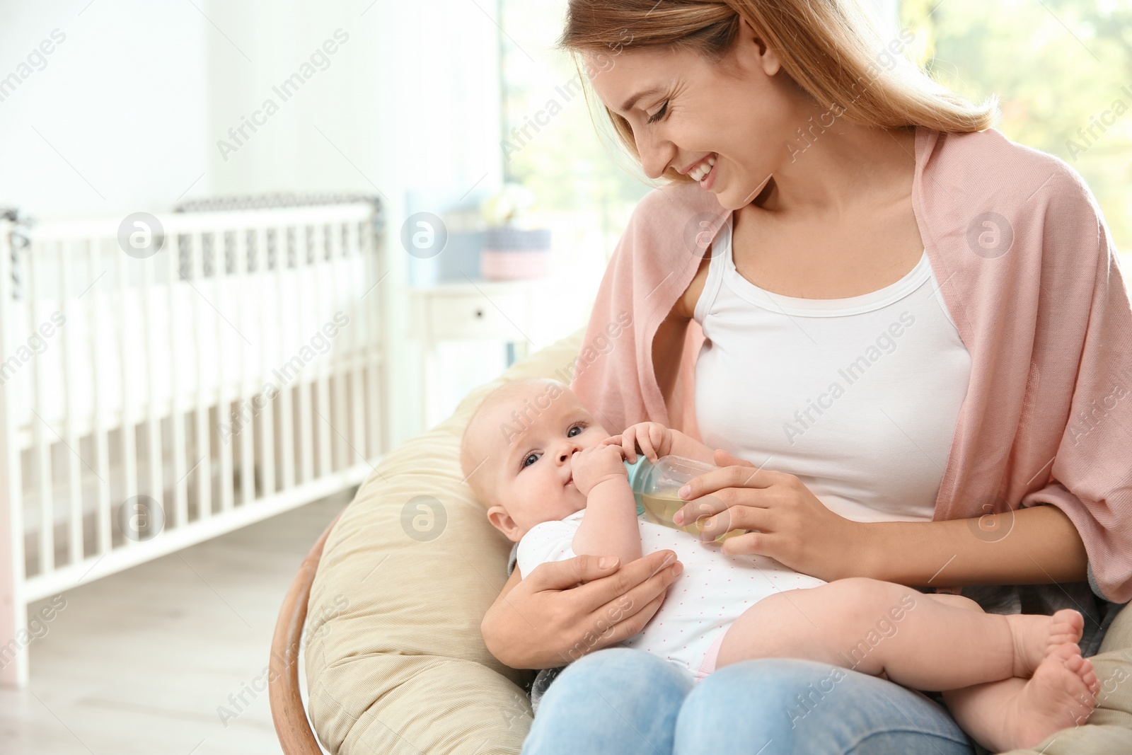 Photo of Lovely mother giving her baby drink from bottle in room. Space for text