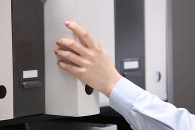 Photo of Woman taking folder with documents from shelf in office, closeup