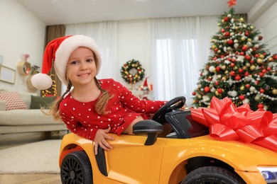 Cute little girl driving toy car in room decorated for Christmas