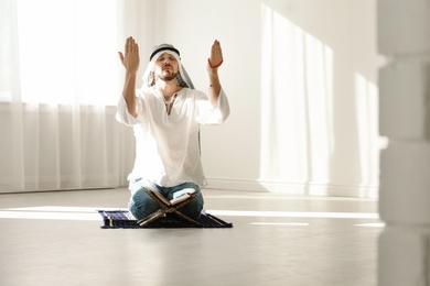 Photo of Muslim man in traditional clothes praying on rug indoors