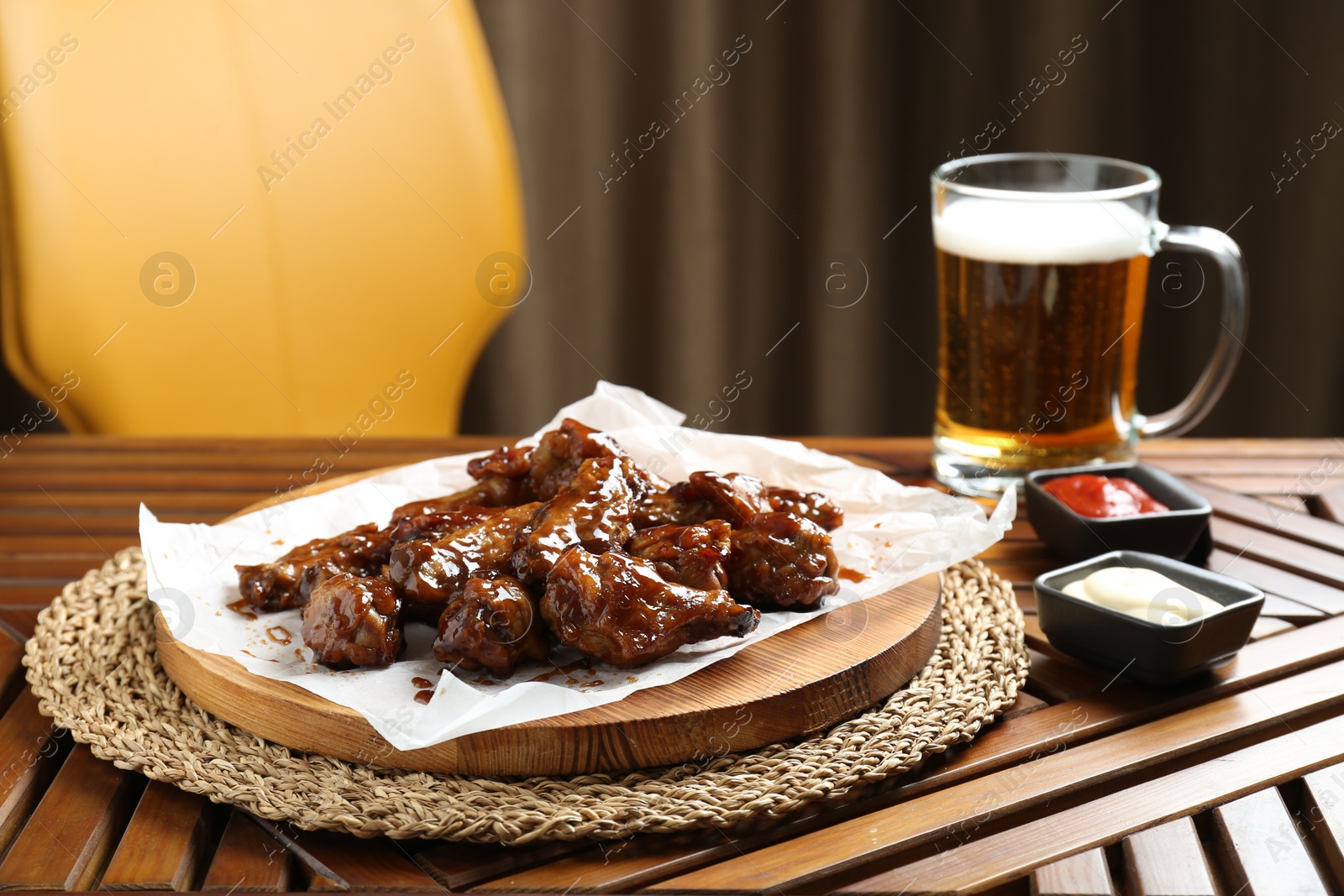 Photo of Tasty chicken wings, sauces and mug of beer on wooden table, space for text. Delicious snack