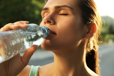 Photo of Young woman drinking water outdoors on hot summer day, closeup. Refreshing drink