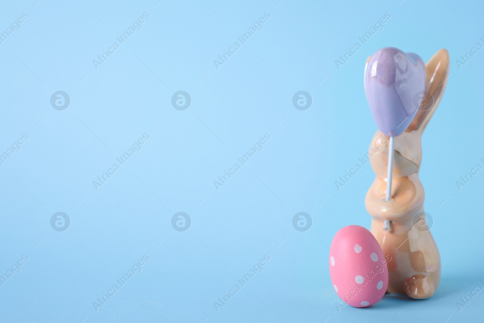 Photo of Easter bunny figure and dyed egg on light blue background. Space for text